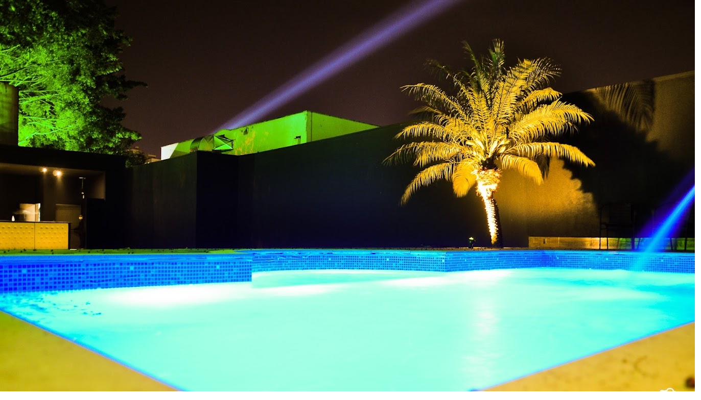Piscina Love Haus com palmeira iluminada e feixe de luz noite