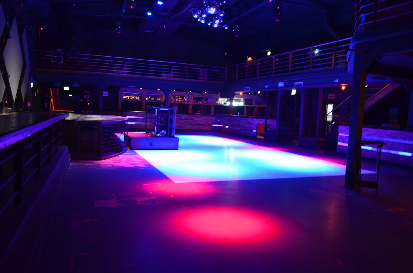Vista ampla do interior da Love Haus em Campinas, mostrando a pista de dança iluminada com luzes LED neon em tons de azul e rosa, estrutura de mezanino de dois andares com guarda-corpo, camarotes ao fundo e cabine de DJ centralizada. Ambiente de balada moderno e amplo, ideal para festas e eventos.